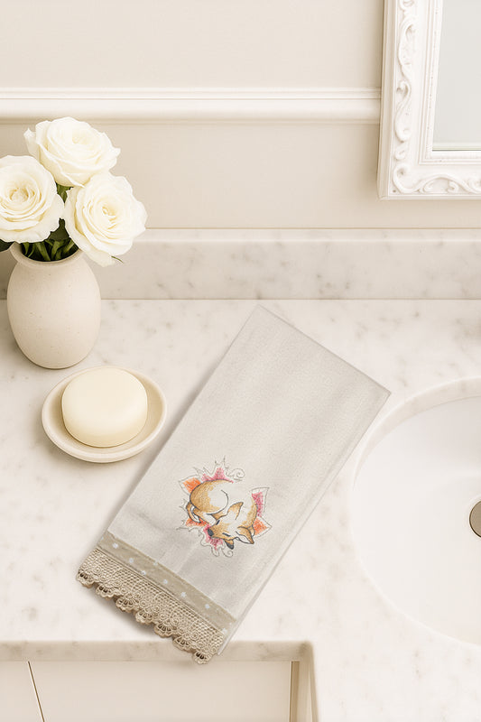 Asciugamano in cotone con ricamo cerbiatto del bosco addormentato tra foglie autunnali, fotografato dall’alto su piano bagno in marmo.