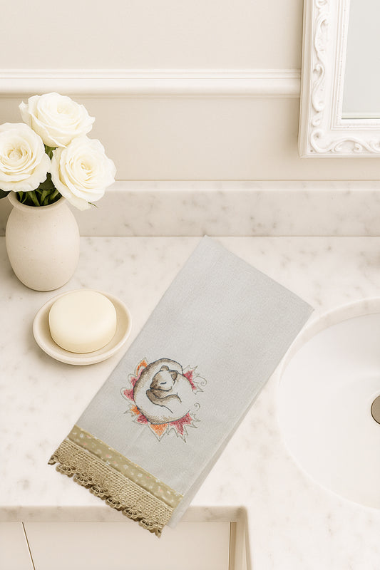 Asciugamano in cotone con ricamo scoiattolo dei sogni avvolto in foglie autunnali, fotografato dall’alto su piano bagno in marmo.