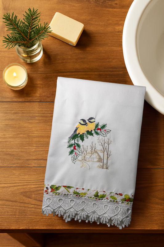Asciugamano Songs of Winter con coppia di cinciallegre ricamate e bordo natalizio, piegato su tavolo in legno con candela e rametto di abete.