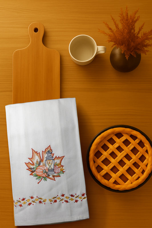 Asciugapiatto Autunno Lanterna con ricamo lanterna autunnale con foglie e decorazioni stagionali, fotografato dall’alto su piano cucina in legno.