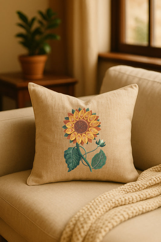 Cuscino decorativo in misto lino beige con ricamo 3D di girasole giallo, appoggiato su un divano chiaro in un ambiente caldo e naturale con pianta sullo sfondo.