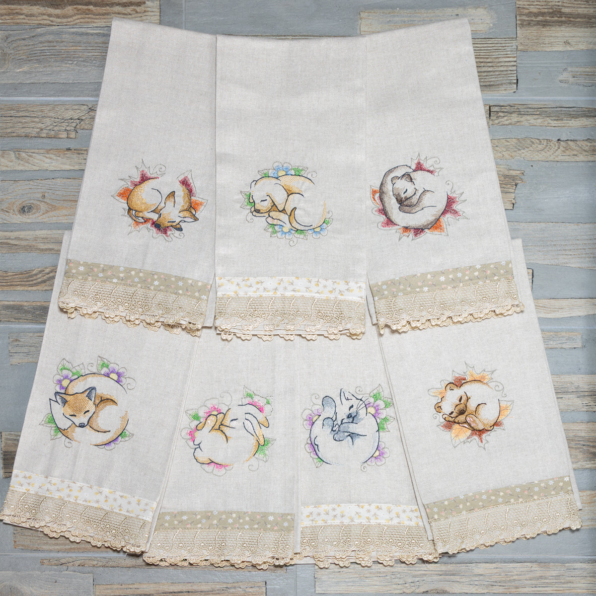 Asciugamani in cotone ricamati con animaletti dormienti della collezione Soffici Ninne, disposti a ventaglio.