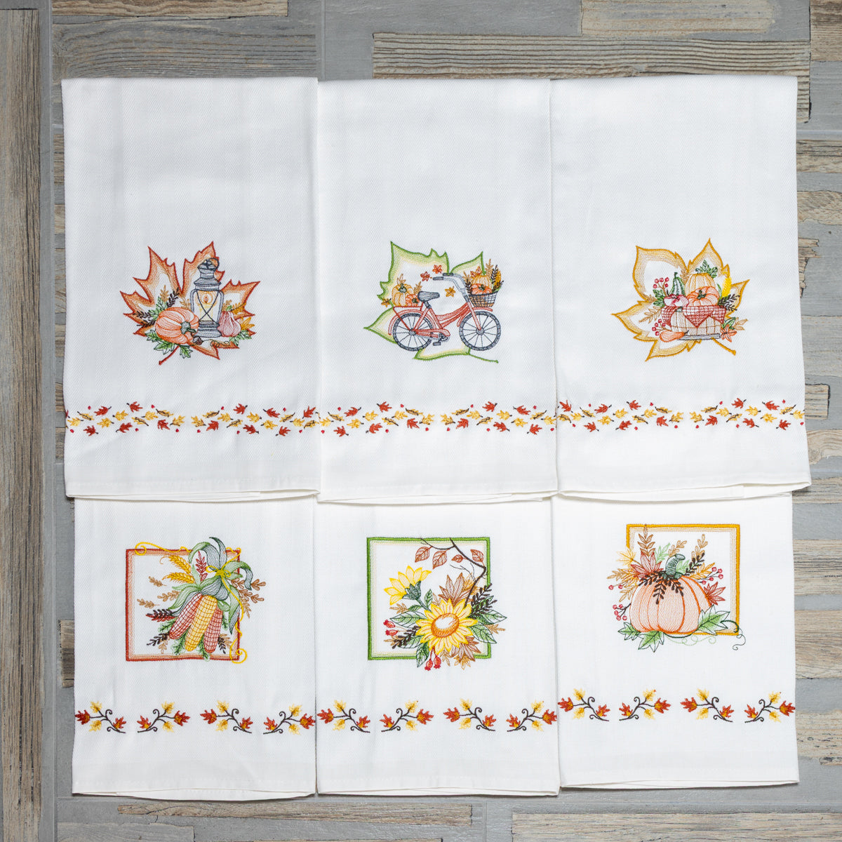 Asciugapiatti ricamati della collezione Autunno Avvolgente con motivi autunnali come zucche, girasoli, pannocchie e lanterne disposti insieme.