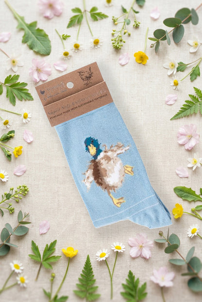 Calza da donna Wrendale Designs in bambù azzurro chiaro con anatra ricamata, fotografata su sfondo primaverile con fiori e foglie.