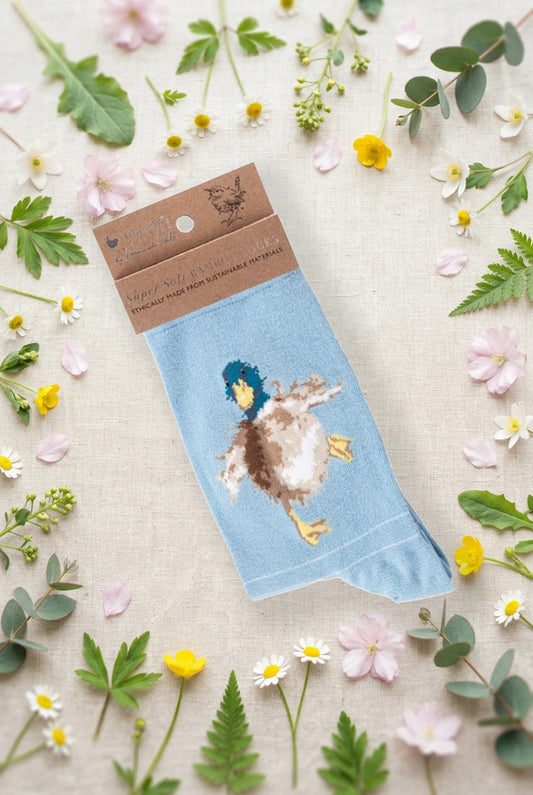Calza da donna Wrendale Designs in bambù azzurro chiaro con anatra ricamata, fotografata su sfondo primaverile con fiori e foglie.