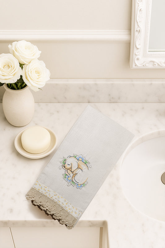 Asciugamano in cotone con ricamo cagnolino addormentato tra fiori azzurri, fotografato dall’alto su piano bagno in marmo.