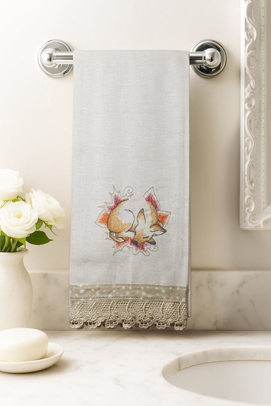 Asciugamano in cotone con ricamo cerbiatto del bosco addormentato tra foglie autunnali, fotografato appeso in un bagno elegante.