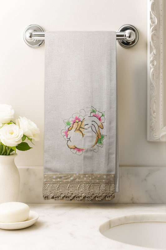 Asciugamano in cotone con ricamo coniglietto sognatore circondato da fiori rosa e verdi, fotografato appeso in un bagno elegante.