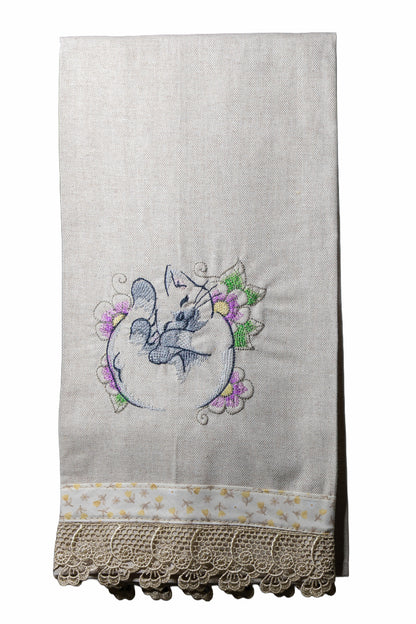 Asciugamano in cotone ricamato con gattino dei fiori arrotolato tra fiori lilla e verdi su sfondo bianco.
