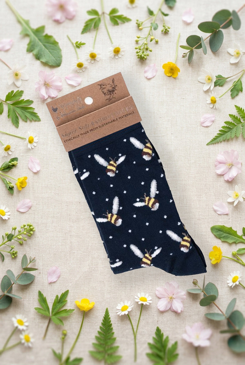 Calza da donna Wrendale Designs in bambù blu navy con pattern di api ricamate, fotografata su sfondo primaverile con fiori e foglie.