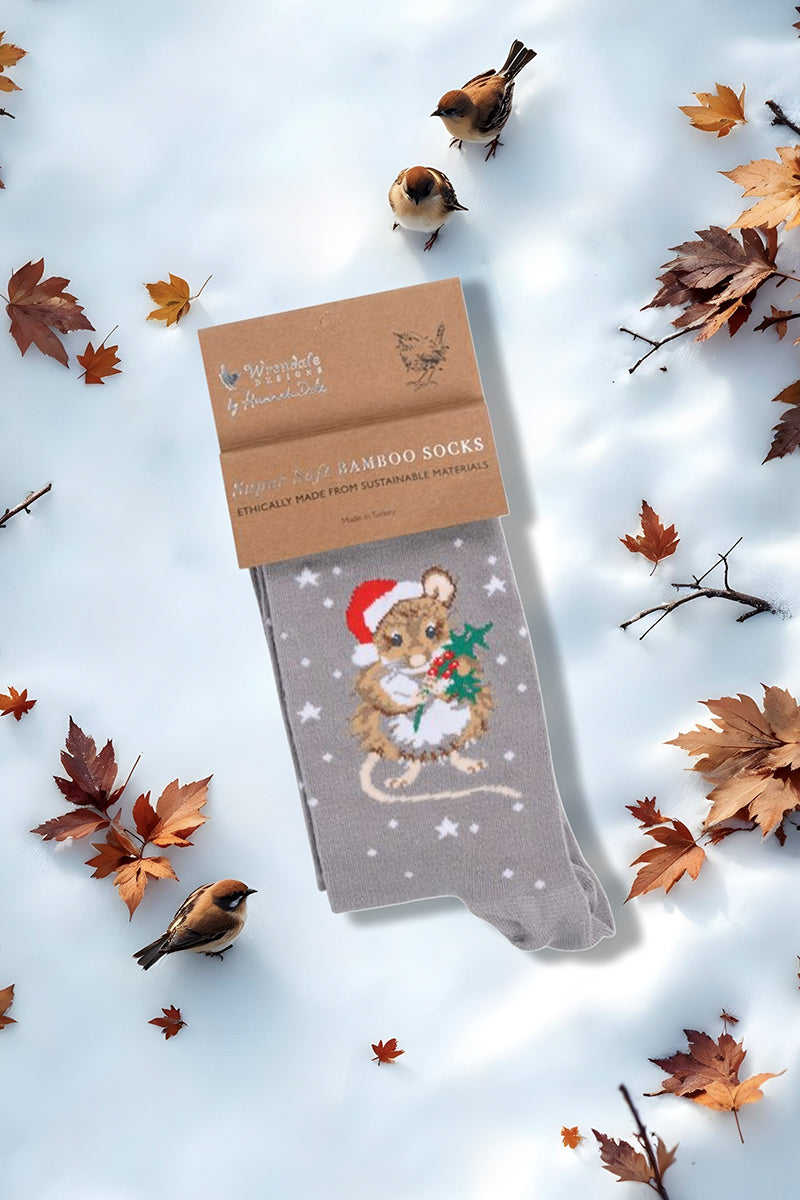 Calza da donna Wrendale Designs in bambù grigio con topolino natalizio ricamato che stringe un rametto di agrifoglio, fotografata su sfondo invernale con neve e foglie secche.