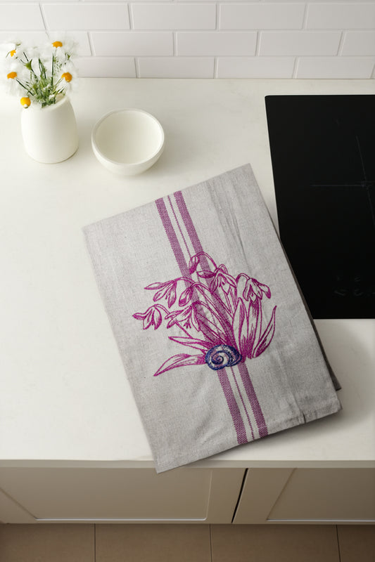 Asciugapiatti ricamato con bucaneve e chiocciola della collezione Vintage Stripes Fleurs Colorées, fotografato dall'alto in cucina moderna.