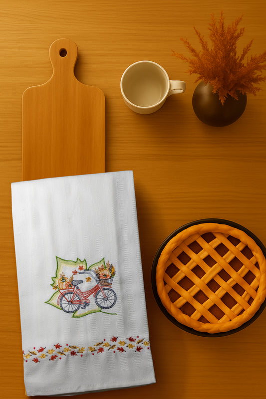Asciugapiatto Autunno Bicicletta con ricamo bicicletta con cestino autunnale e foglie colorate, fotografato dall’alto su piano cucina in legno.