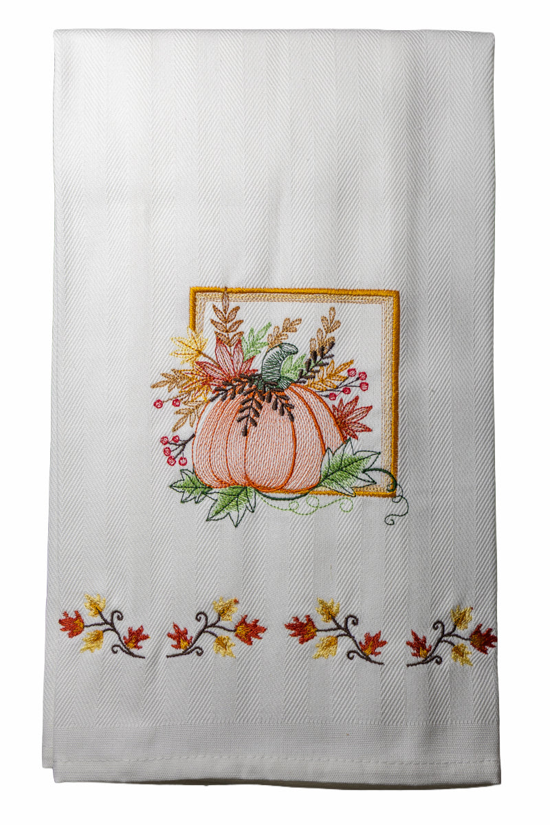 Ricamo zucca autunnale con foglie e bacche su asciugapiatto in cotone bianco, fotografato su sfondo neutro.