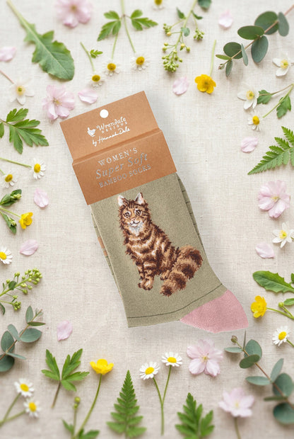 Calza da donna Wrendale Designs in bambù verde chiaro a righe con gatto soffice tigrato ricamato, fotografata su sfondo primaverile con fiori e foglie.