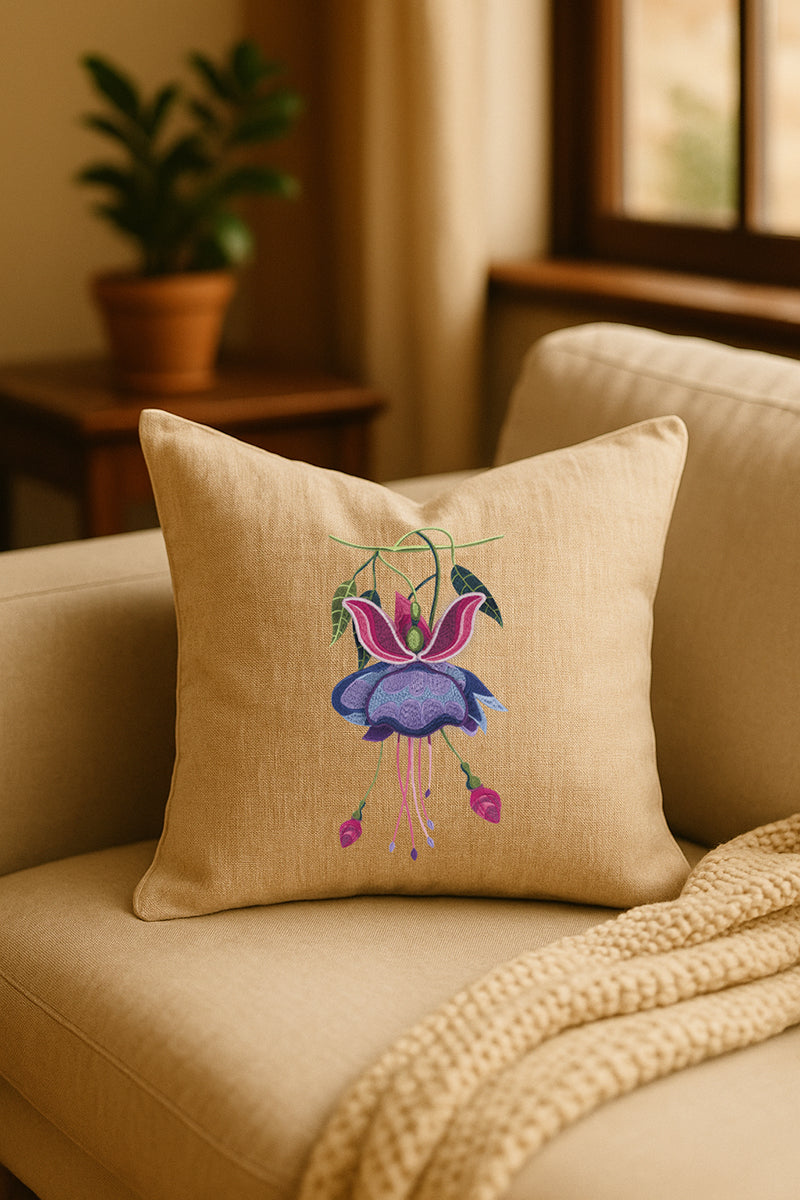 Cuscino decorativo in misto lino beige con ricamo tridimensionale di fucsia viola, appoggiato su un divano chiaro in un ambiente caldo e naturale con pianta sullo sfondo.