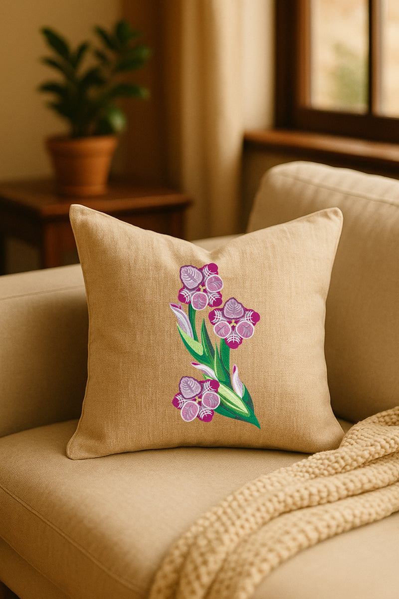Cuscino decorativo in misto lino beige con ricamo tridimensionale di gladiolo rosa, appoggiato su un divano chiaro in un ambiente caldo e naturale con pianta sullo sfondo.