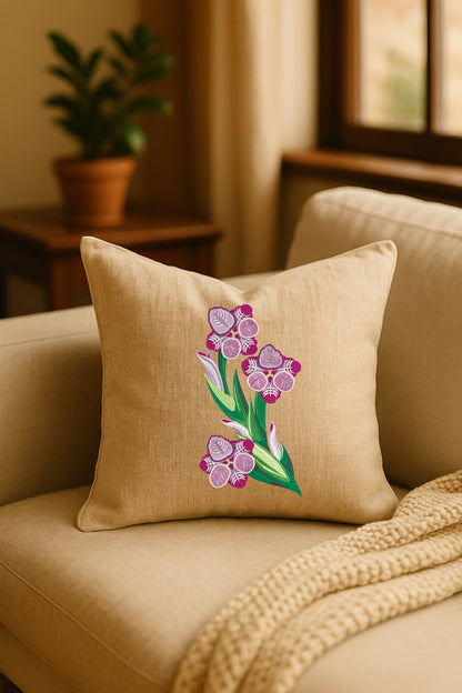 Cuscino decorativo in misto lino beige con ricamo tridimensionale di gladiolo rosa, appoggiato su un divano chiaro in un ambiente caldo e naturale con pianta sullo sfondo.