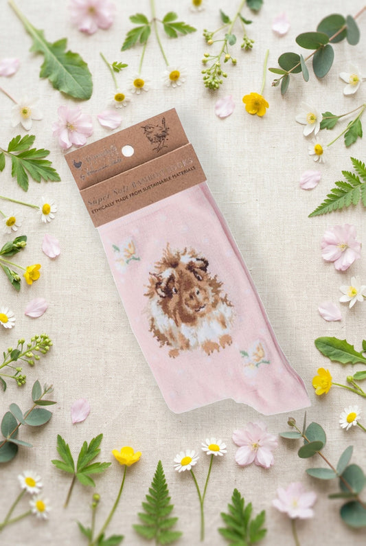Calza da donna Wrendale Designs in bambù rosa cipria con porcellino d'India ricamato e fiorellini, fotografata su sfondo primaverile con fiori e foglie.