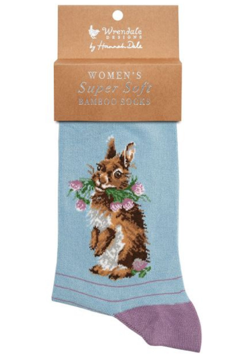 Calza da donna Wrendale Designs in bambù azzurro con ricamo di coniglio marrone che tiene un mazzolino di trifogli rosa, presentata con cartoncino kraft del brand su sfondo neutro.