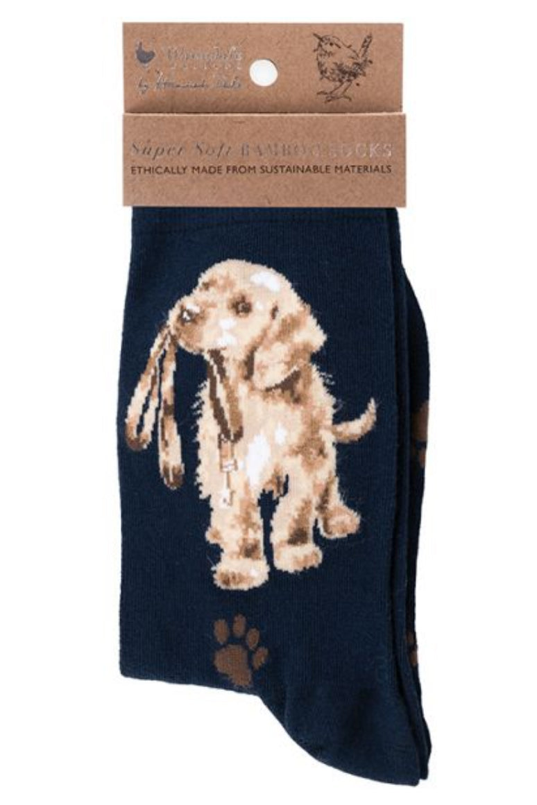 Calza da donna Wrendale Designs in bambù blu navy con ricamo di cucciolo di labrador che tiene il guinzaglio in bocca, presentata con cartoncino kraft del brand su sfondo neutro.