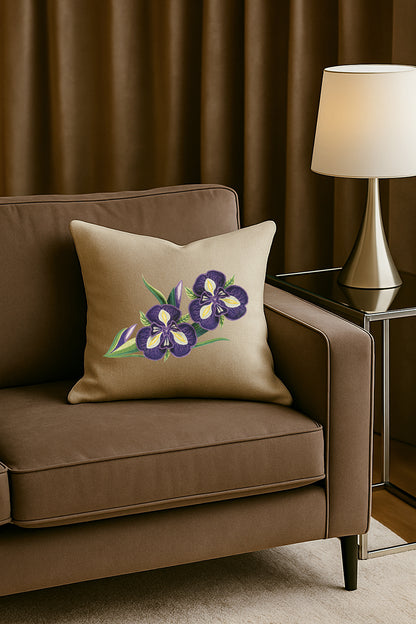 Cuscino in misto lino beige con ricamo 3D di iris viola, posato su un divano marrone in un soggiorno elegante con lampada dorata e tende scure.
