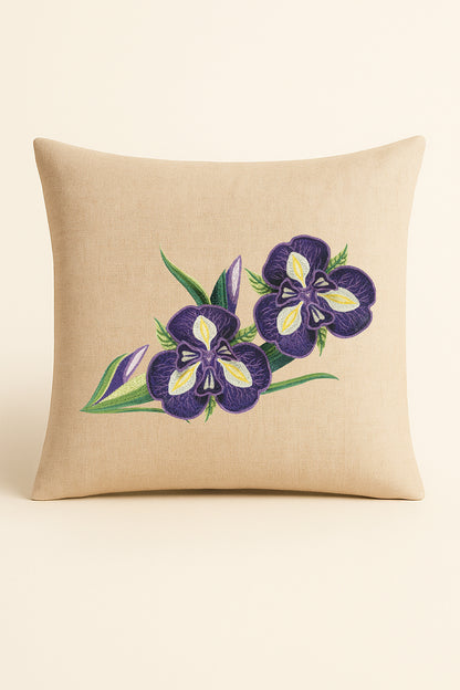 Cuscino quadrato in misto lino beige fotografato su sfondo neutro, con ricamo 3D di iris viola e foglie verdi in stile artigianale.