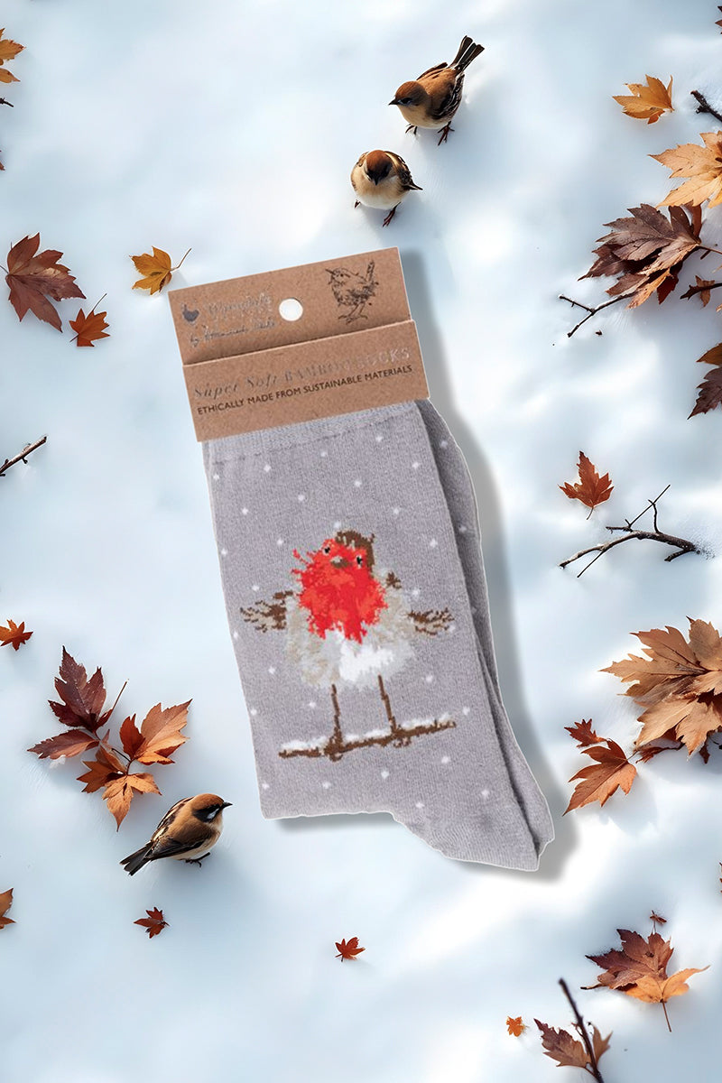 Calza da donna Wrendale Designs in bambù grigio con pettirosso gioioso ricamato, fotografata su sfondo invernale con neve, foglie secche e uccellini.