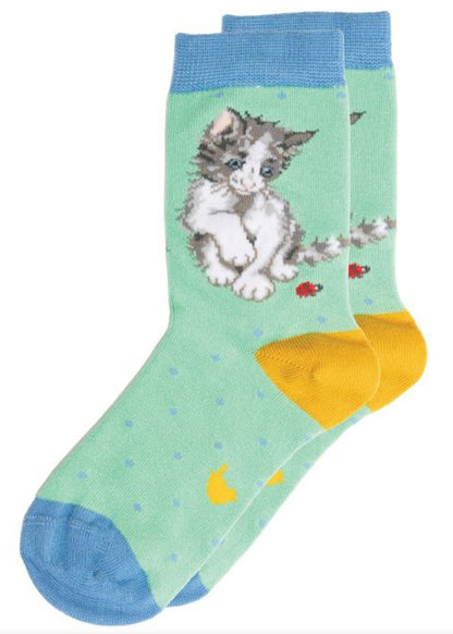Coppia di calze Wrendale Designs da bambini in verde menta con polsino e punta azzurri e tallone giallo, decorate con gattino che gioca con coccinelle, su sfondo bianco.