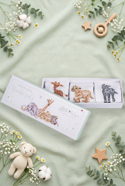 Scatolina regalo Wrendale Designs per neonati decorata con animali della savana: giraffa, elefantino e zebra, contenente tre paia di calzini ricamati, posizionata su fondo verde salvia primaverile con foglie, fiori e giochini.