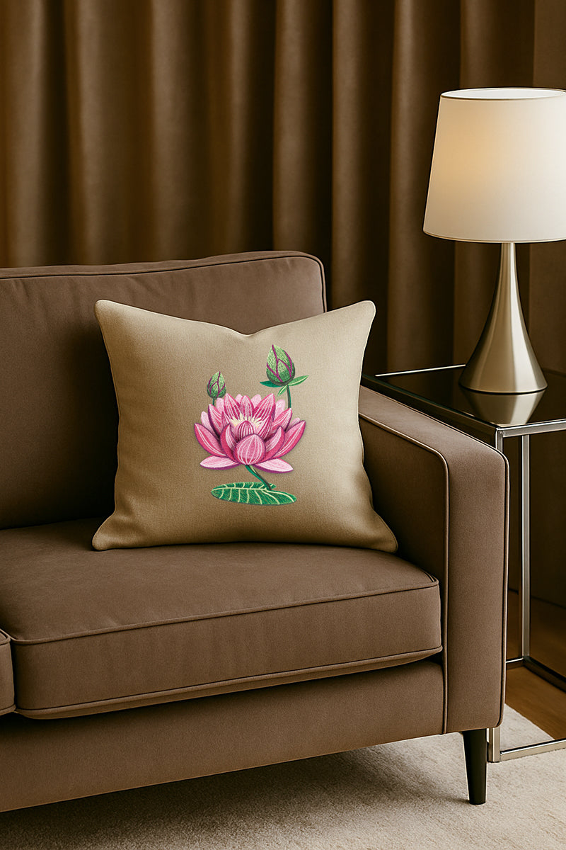 Cuscino in misto lino beige caldo con ricamo tridimensionale di un fiore di loto rosa, appoggiato su un divano moderno color cioccolato in un soggiorno elegante con lampada dorata e tende scure.