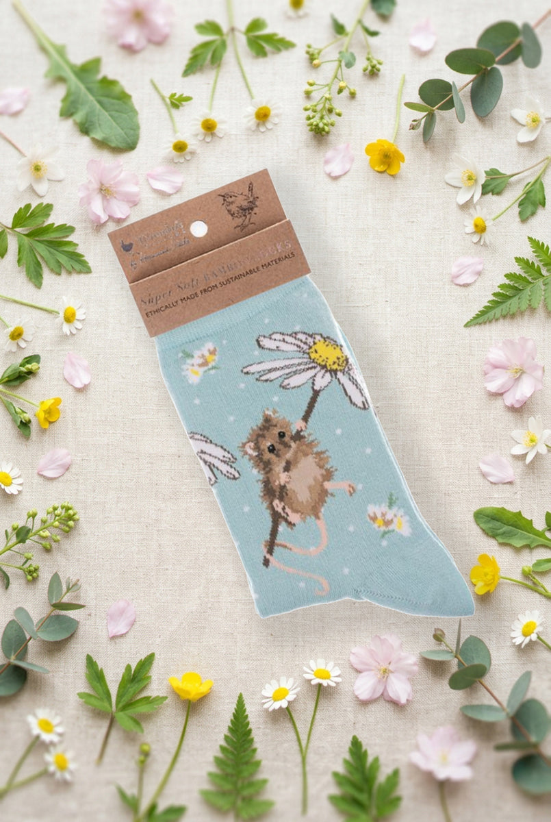 Calza da donna Wrendale Designs in bambù verde acqua con topolino su margherita ricamato e pois bianchi, fotografata su sfondo primaverile con fiori e foglie.