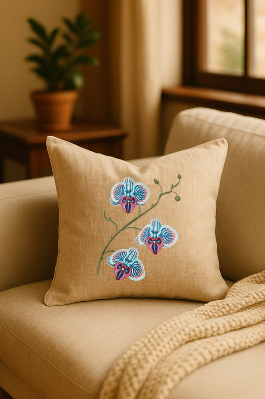 Cuscino decorativo in misto lino beige con ricamo 3D di orchidea blu, turchese e porpora, appoggiato su un divano chiaro in un ambiente naturale con pianta sullo sfondo.