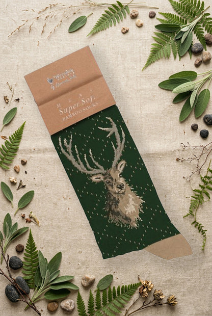 Calza da uomo Wrendale Designs in bambù verde scuro con illustrazione di un cervo con palco imponente, fotografata su sfondo naturale primaverile.