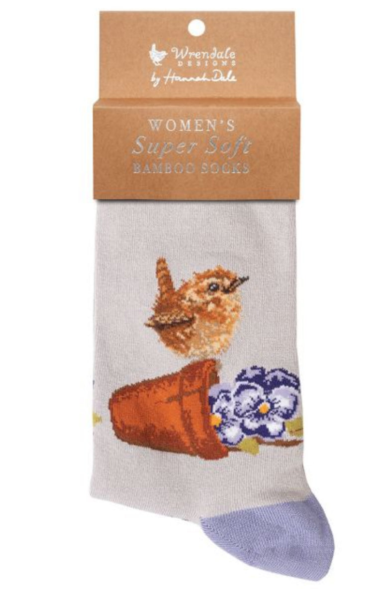 Calza da donna Wrendale Designs in bambù beige chiaro con ricamo di Scricciolo su vaso di terracotta rovesciato accanto a violette, presentata con cartoncino kraft del brand su sfondo neutro.