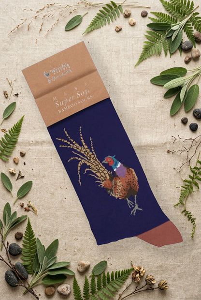 Calza da uomo Wrendale Designs in bambù blu notte con illustrazione di un fagiano colorato, fotografata su sfondo naturale primaverile.