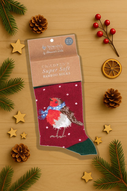 Calza Wrendale Designs da bambini in rosso con pettirosso natalizio, fotografata in ambientazione festiva con pigne, stelline in legno e rametti di abete.