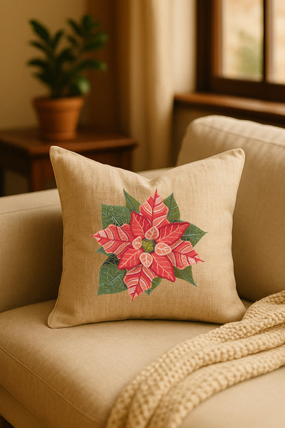 Cuscino decorativo in misto lino beige con ricamo 3D di stella di Natale rossa e foglie verdi, appoggiato su un divano chiaro in un ambiente naturale con pianta sullo sfondo.