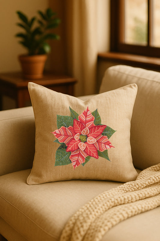 Cuscino decorativo in misto lino beige con ricamo 3D di stella di Natale rossa e foglie verdi, appoggiato su un divano chiaro in un ambiente naturale con pianta sullo sfondo.