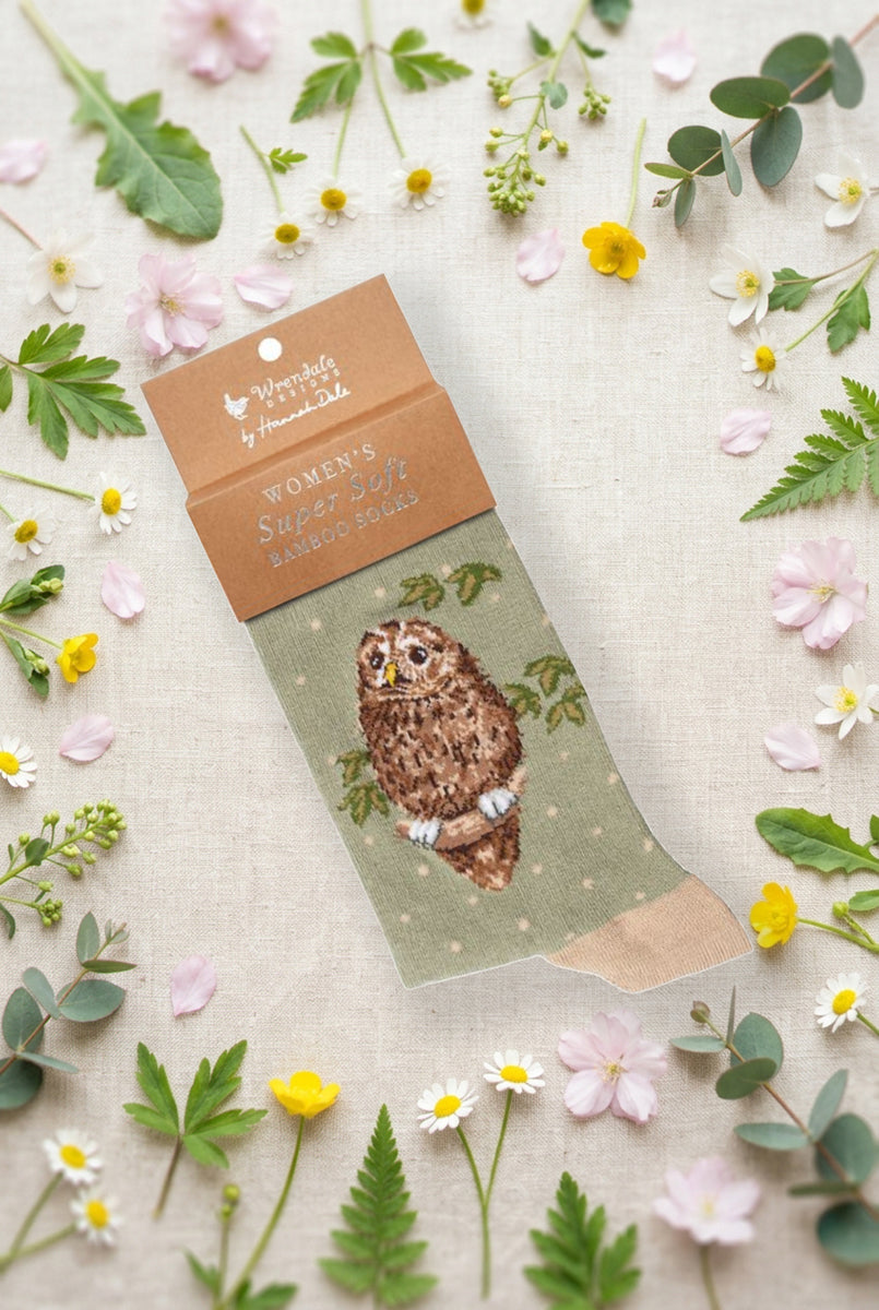 Calza da donna Wrendale Designs in bambù verde salvia con gufetto e foglie ricamate e piccoli pois chiari, fotografata su sfondo primaverile con fiori e foglie.