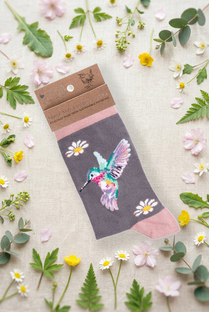 Calza da donna Wrendale Designs in bambù grigio con colibrì multicolore ricamato e margherite, fotografata su sfondo primaverile con fiori e foglie.